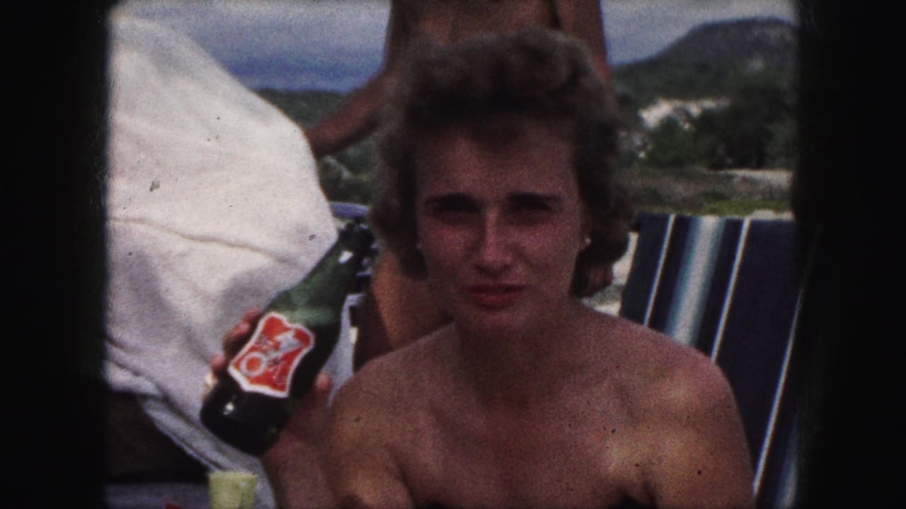 Woman in a black strapless swimsuit seated outdoors holding a green bottle with a red label.