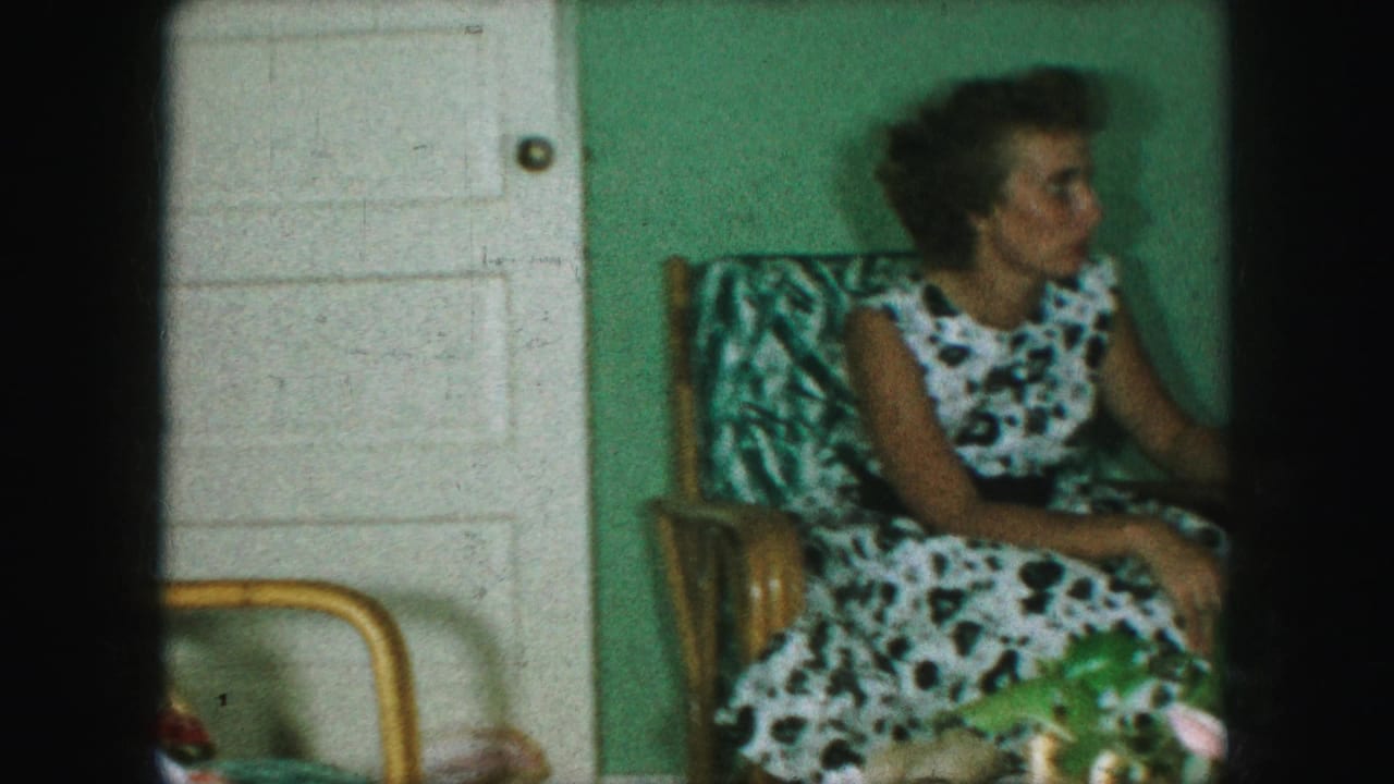 Woman in a patterned chair turns to the side near a white paneled door.