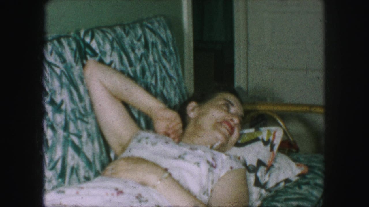 In supported 1959 Kansas City home-movie footage, an adult woman rests on a green-and-white patterned sofa in a floral dress.
