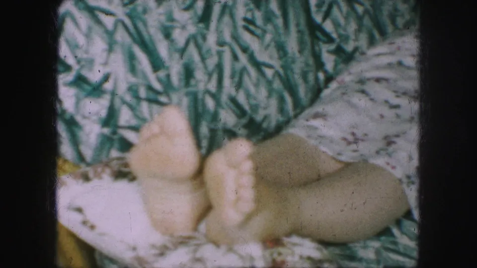 A close home-movie view shows the woman reclining lengthwise, with bare feet in the foreground and patterned upholstery behind her.
