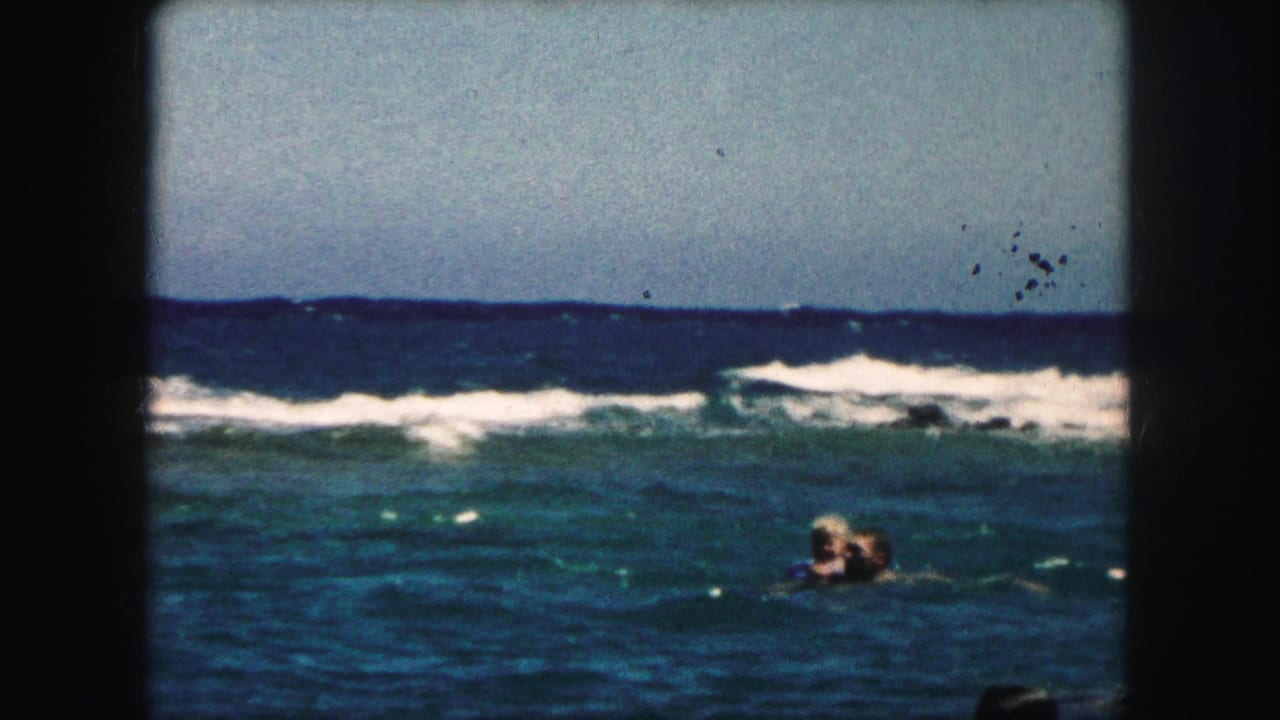 1959 8mm frame of swimmers in ocean water, with low waves, bright sky, and rounded film-frame edges.