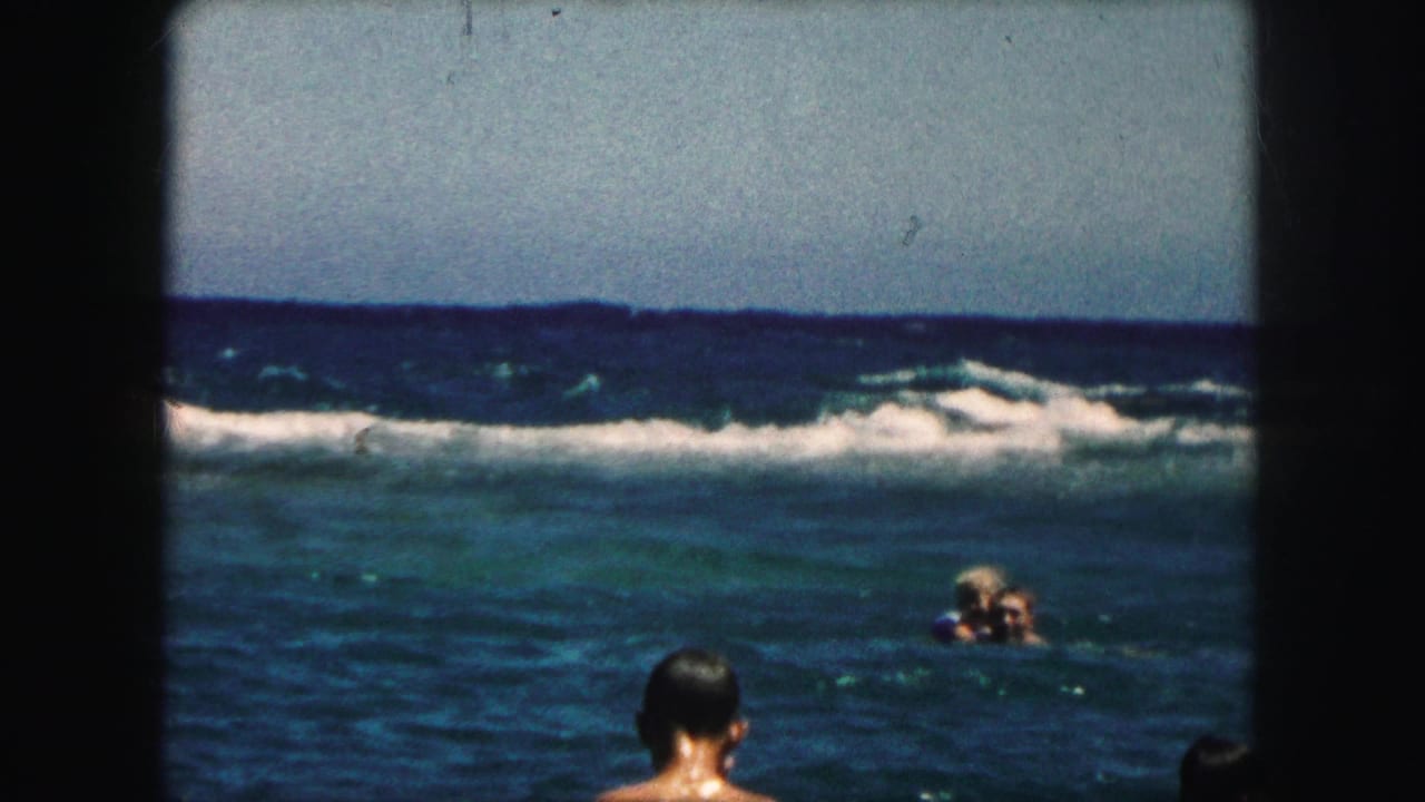 Swimmers in the ocean with a foreground swimmer seen from behind.
