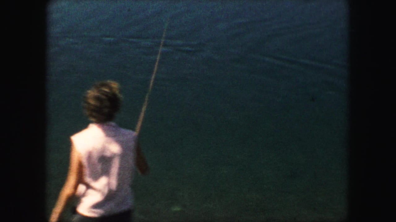 Person in a light sleeveless shirt holds a fishing rod beside blue-green water.