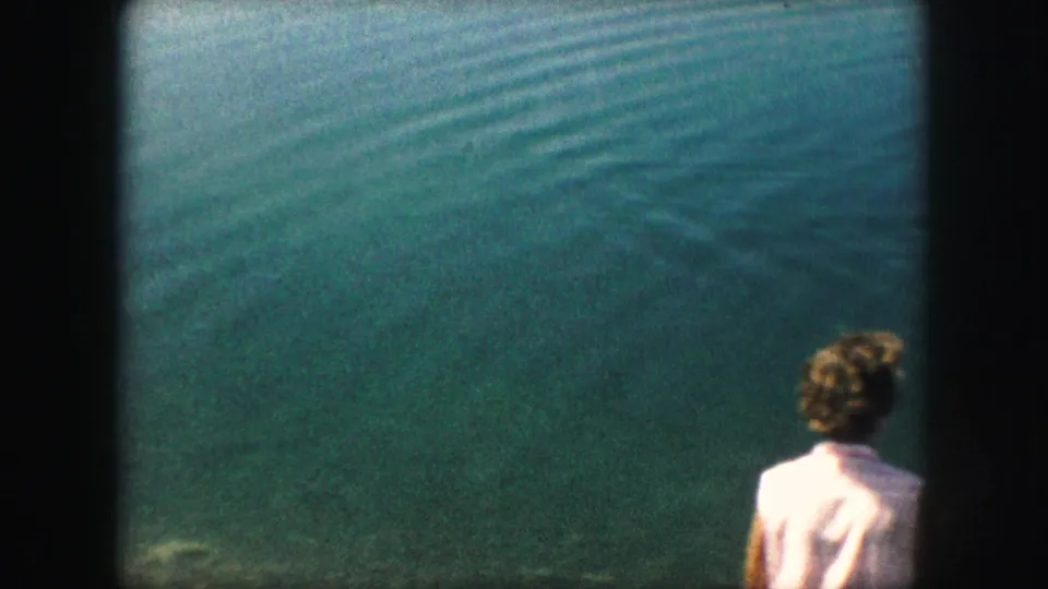 1959 8mm frame with the person partly cropped at right and wide blue-green water filling most of the view.