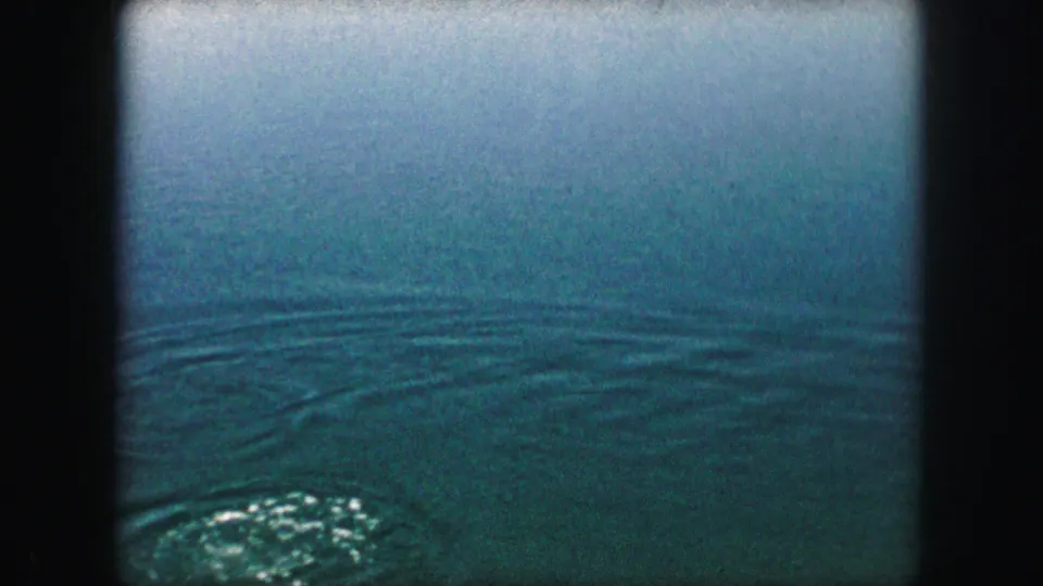 1959 8mm frame focused on rippled water, with a small white foamy patch near the bottom of the frame.