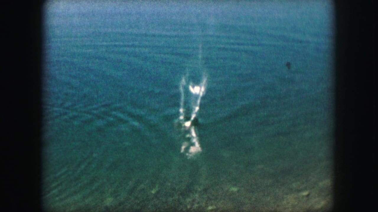 Rippling pond water with a small splash and a partial arm near the surface.