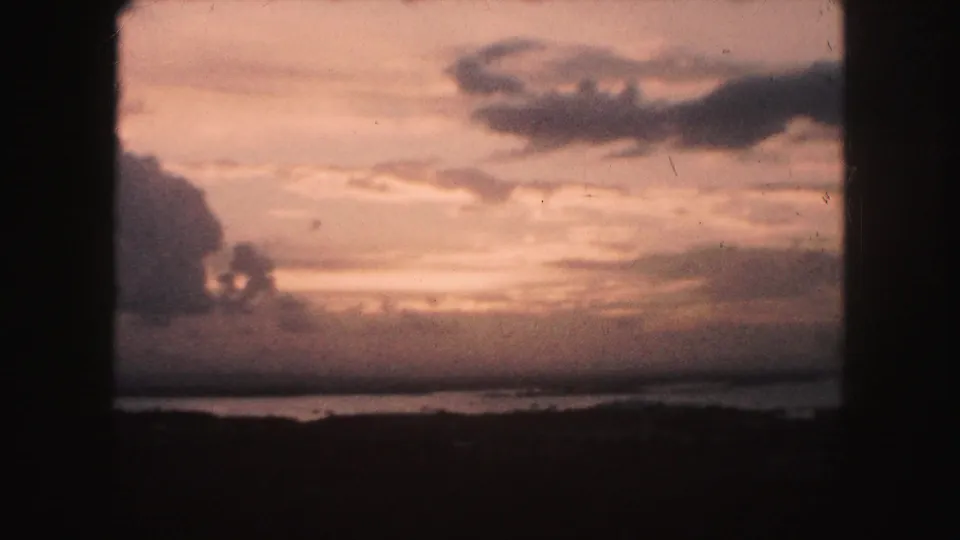 1959 Kansas City area 8mm frame showing a pink-orange sunset over water, with a low shoreline and dark projector-frame edges.