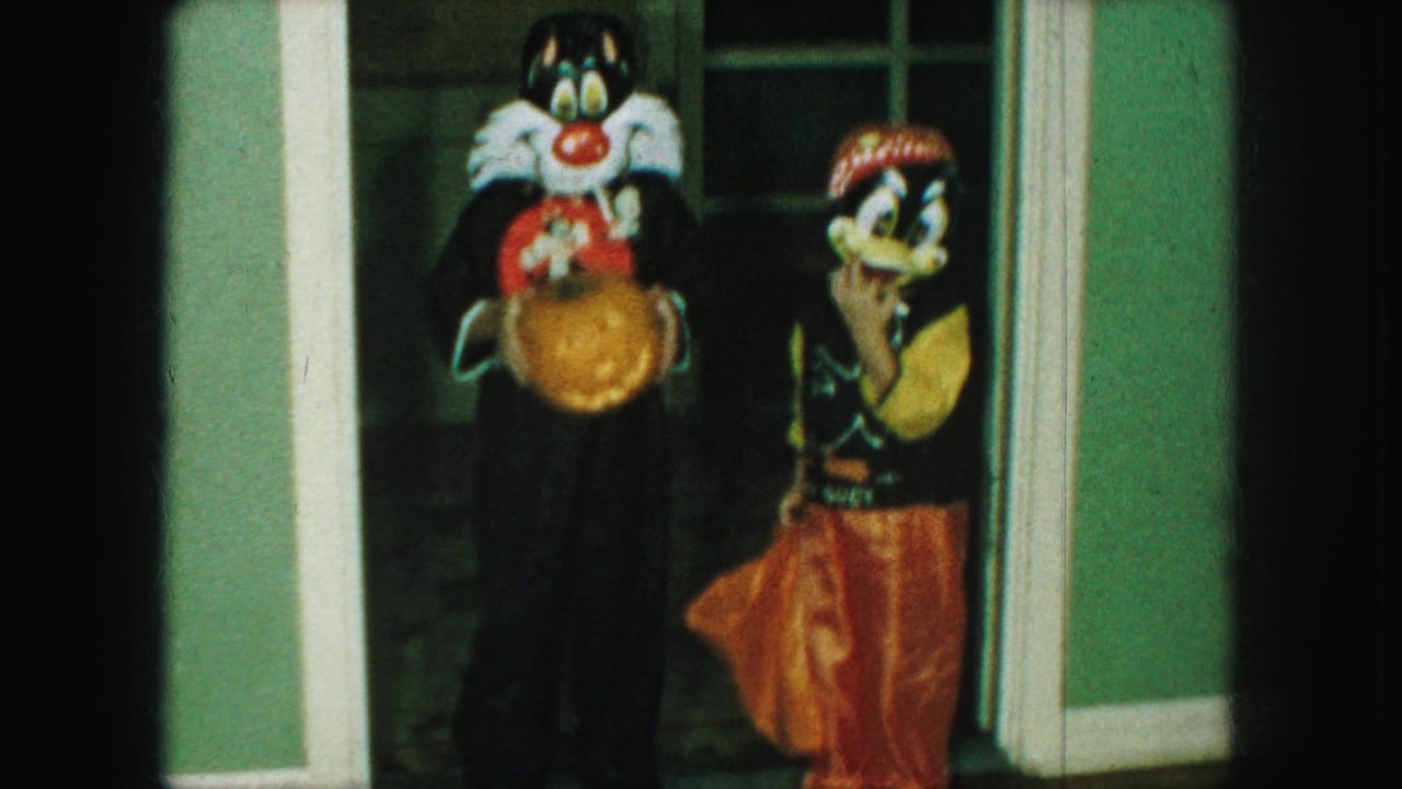 Two children in cartoon Halloween costumes stand side by side at a doorway.