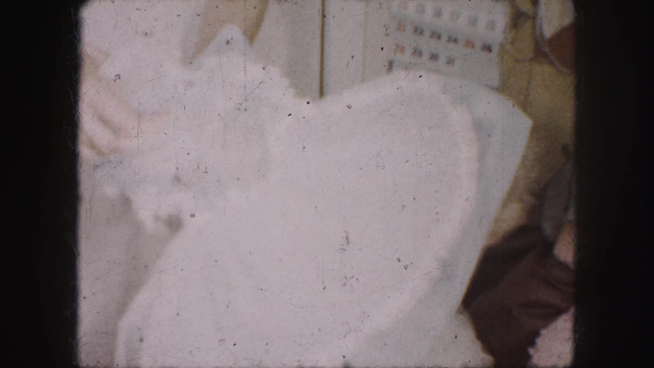 1959 Kansas City interior frame with a white dress held close to camera and a partially visible person near a wall calendar.