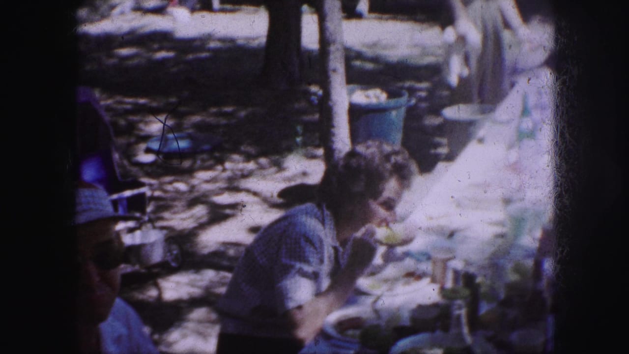 A 1959 Kansas City picnic frame shows a woman seated outdoors, eating at a table with plates, cups, trees, and a blue trash can nearby.
