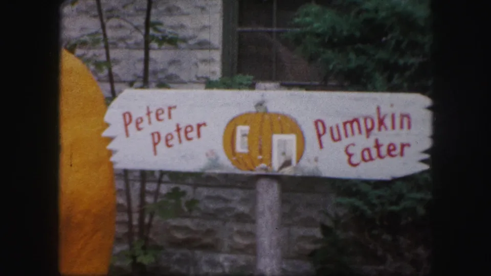 1959 Kansas City 8mm frame showing a hand-painted Peter Peter Pumpkin Eater sign in front of a stone wall and greenery.