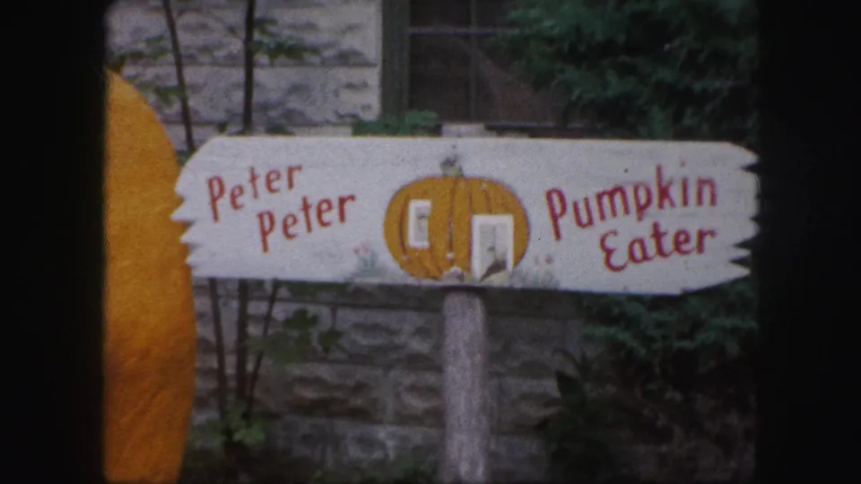 1959 Kansas City 8mm still showing the seasonal Peter Peter Pumpkin Eater sign mounted on a post before a stone wall.