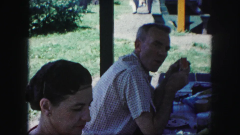 At a Kansas City picnic in 1959, an older man holds food at the table while the woman sits closer to the camera.