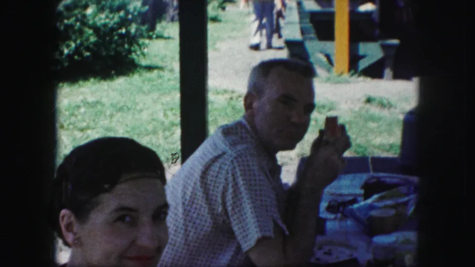 The woman glances toward the camera in a 1959 Kansas City picnic scene while the older man sits behind her with food.