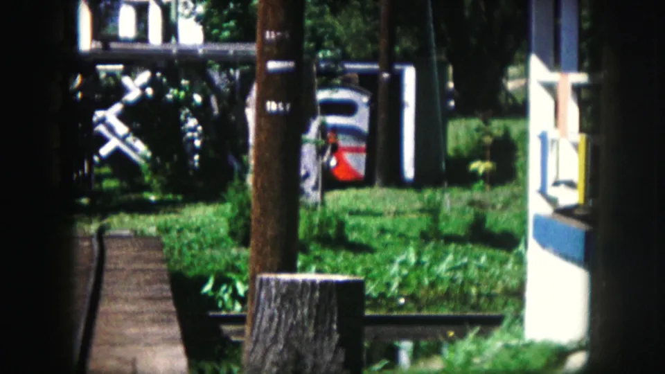 A small park railway track runs through green grass with posts and a train car in 1959 Kansas City footage.