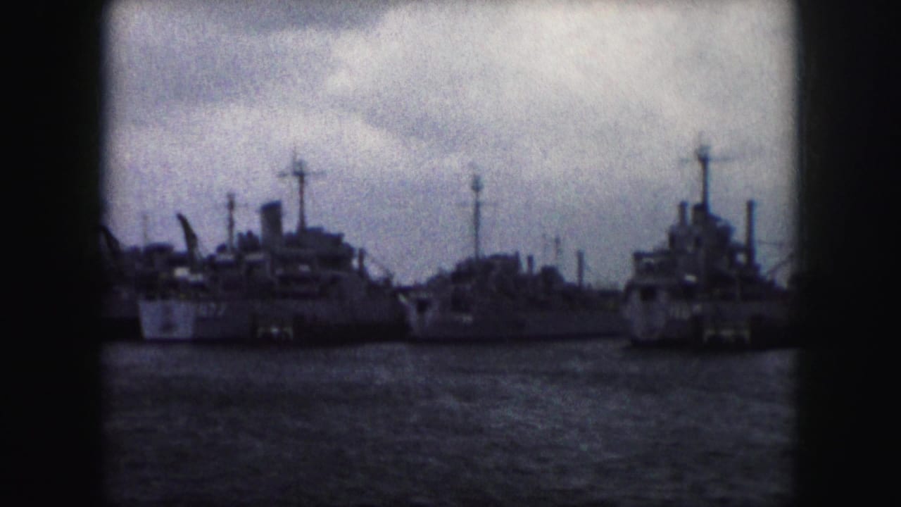 1959 home-movie frame with a cluster of moored ships, visible funnels, masts, and superstructures along the waterfront.