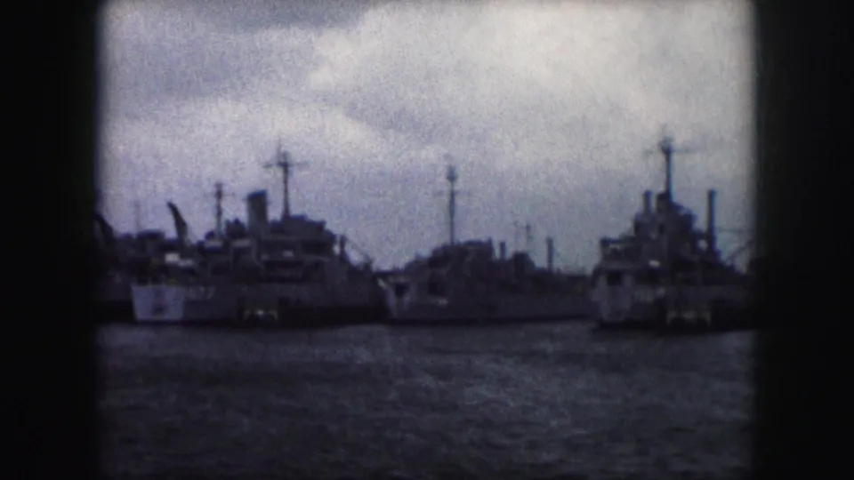 1959 home-movie frame with a cluster of moored ships, visible funnels, masts, and superstructures along the waterfront.