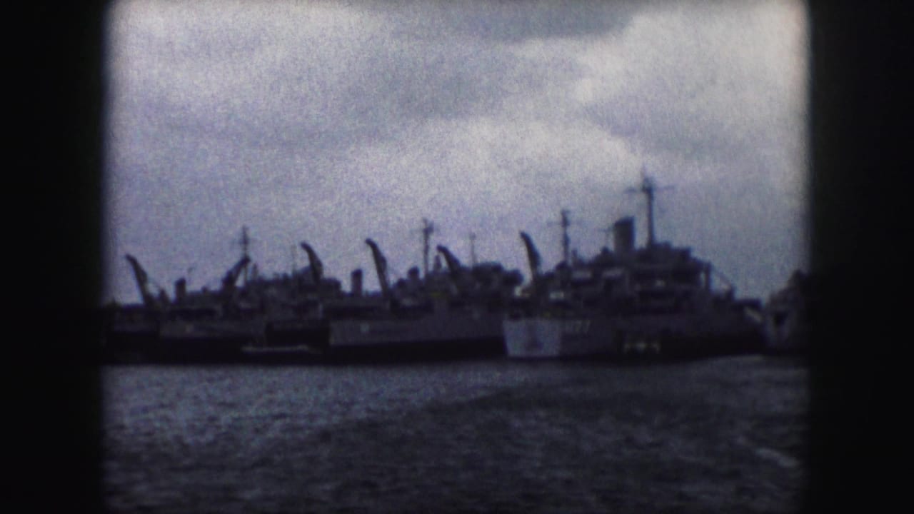 A distant 1959 waterfront view shows several moored naval vessels and vertical ship structures under heavy clouds.