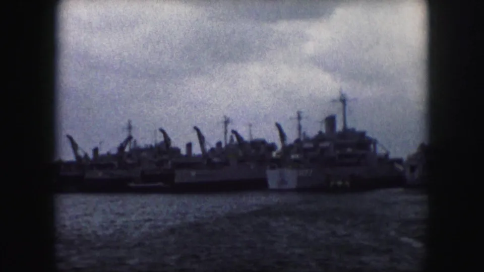 A distant 1959 waterfront view shows several moored naval vessels and vertical ship structures under heavy clouds.
