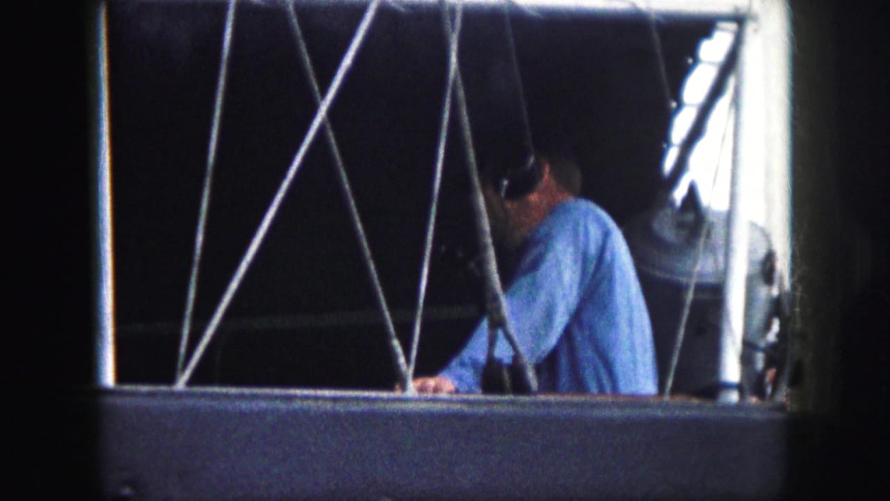 Man in blue shirt remains partly turned away behind crossed cables and a bright window edge.