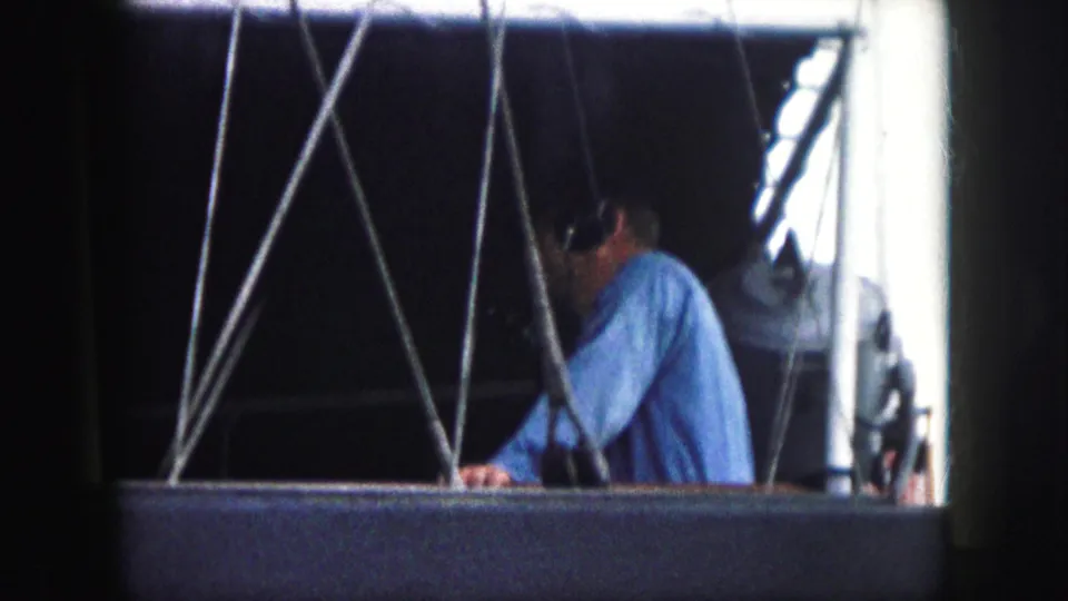 A 1959 8mm frame shows the man leaning within the cable-braced opening, with soft grain and bright side light visible.