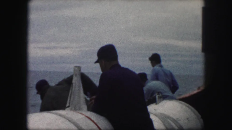 A rear view shows men in caps gathered around white deck equipment during the 1959 8mm boat scene.