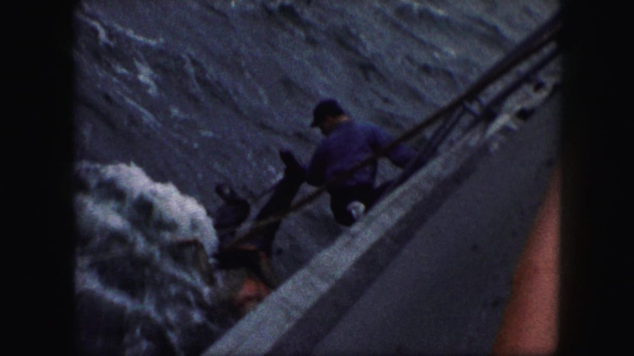1959 8mm home-movie frame showing a man on a boat reaching down toward a person in rough water, with dark film borders visible.