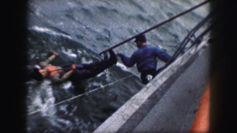 Final 8mm frame shows the man in the water beside the boat, with a rope crossing the water and the rescuer positioned above the rail.