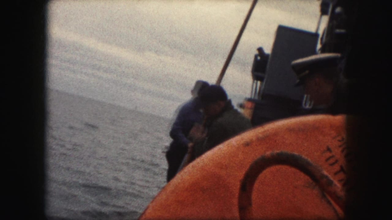 1959 8mm frame showing sailors on a ship deck near the rail, with an orange life preserver in the foreground and open water beyond.
