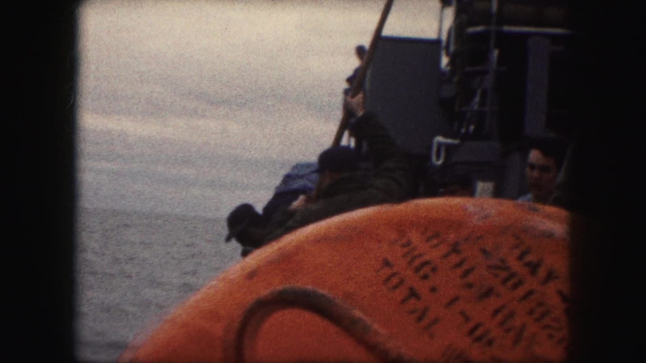 Men in uniform lean over a ship deck area beside a large orange life preserver.