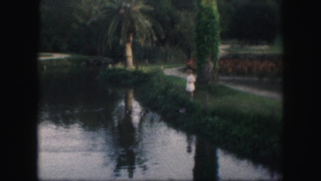 A light-dressed park visitor stands near the water beside plantings and a path in 1959 Kansas City home-movie footage.