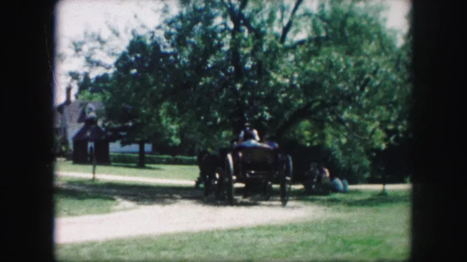 1959 Kansas City home-movie frame showing a horse-drawn wagon moving along a dirt path in a green park-like setting.
