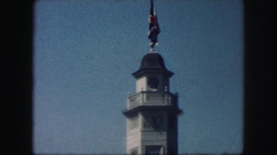 The final 1959 frame cuts to a tall clock-tower structure with a flag above it, seen from below against open sky.