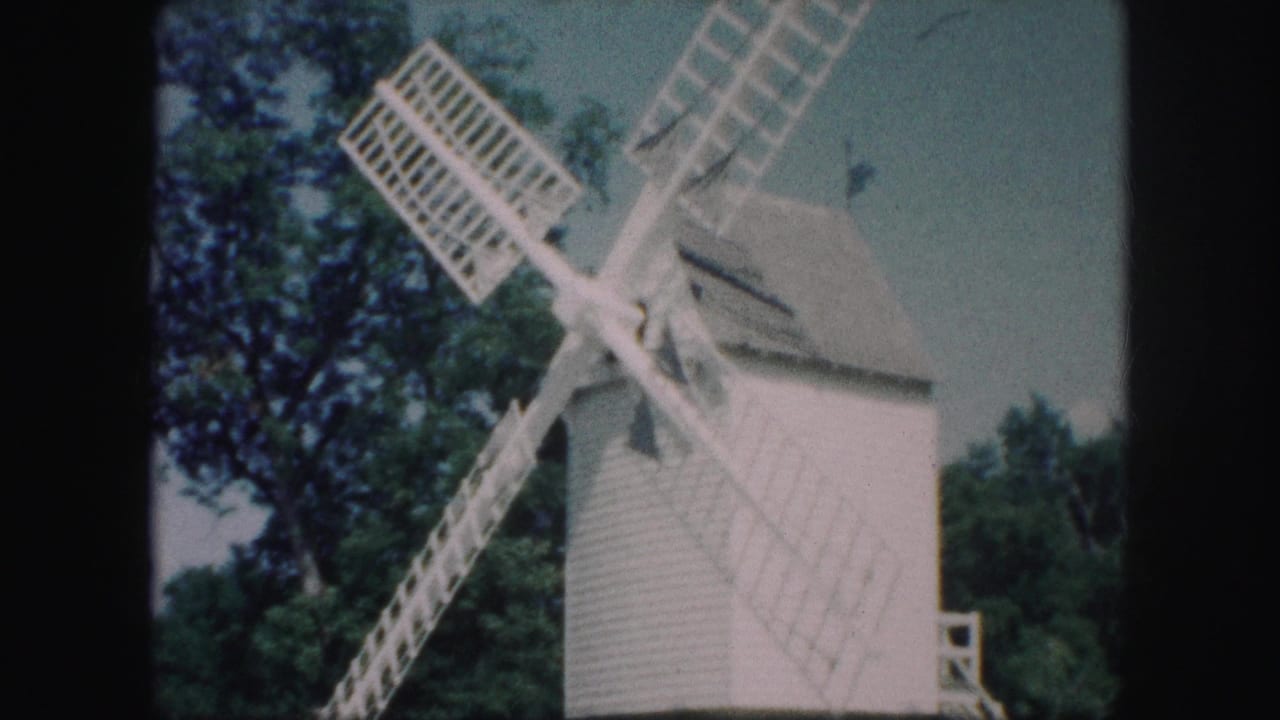 1959 Kansas City footage frame with the windmill blades angled across a pale sky and leafy trees behind the white structure.