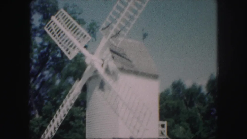 1959 Kansas City home-movie frame showing the white windmill from a low angle as its lattice blades blur across the sky.