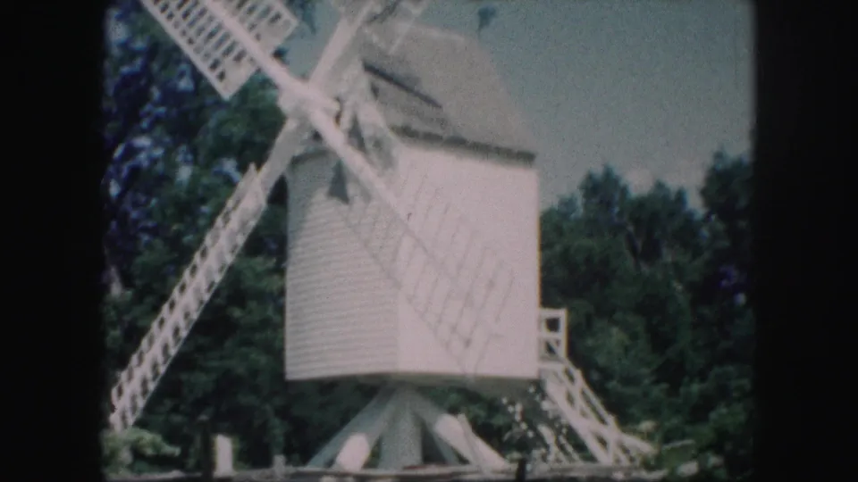 Kansas City 1959 frame of a white windmill, its lattice blades crossing in front of trees and a small stairway.