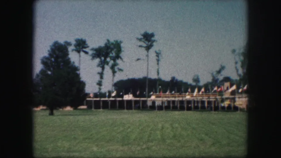 1959 Kansas City home-movie view of an outdoor flag display on a raised platform, with lawn and tall trees around it.