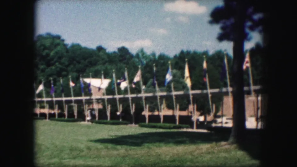 The final 1959 Kansas City frame shows flags around the field, tree shade on the grass, and a partial vehicle near the right edge.