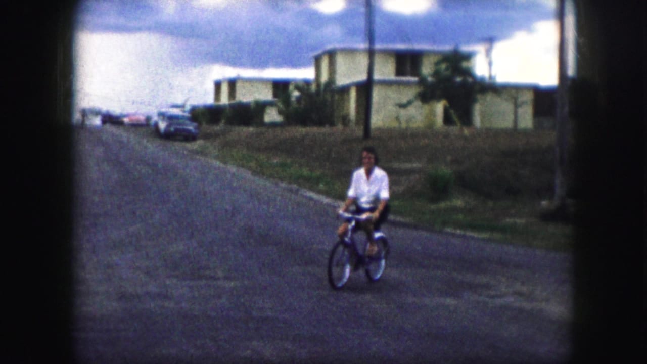 Woman riding a bicycle down the middle of a residential street toward the camera.