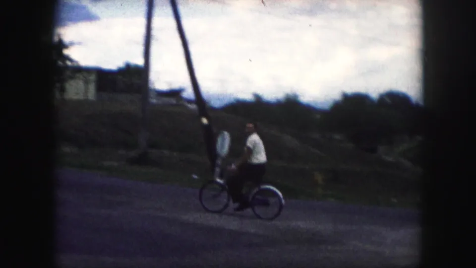 Two riders travel together on bicycles along a quiet Kansas City street, framed by utility poles and dark 8mm edges.