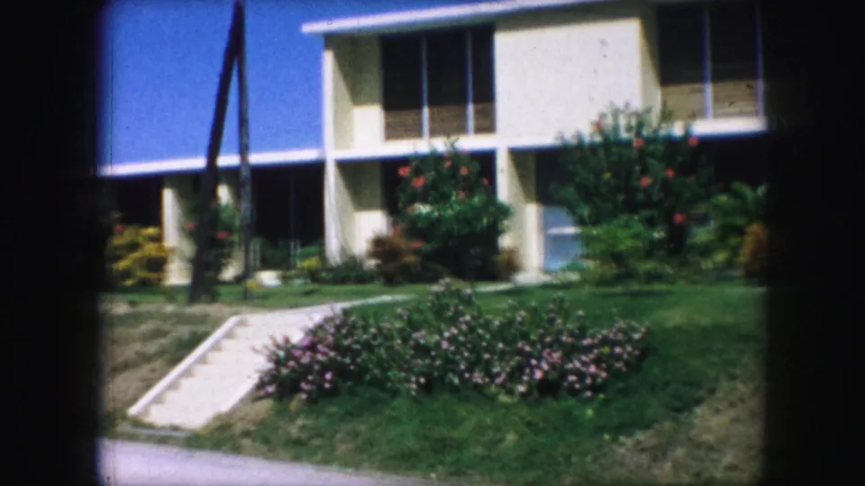 1959 Kansas City home exterior with concrete steps, walkway, flower beds, shrubs, and a cream mid-century house facade.