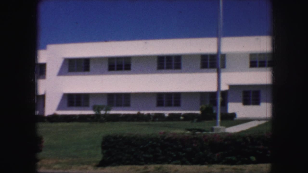 A 1959 Kansas City exterior shows a white multi-story building, flagpole, lawn, and hedge in soft 8mm color.