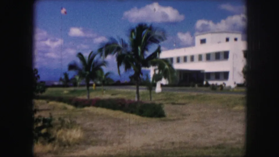 A wider 1959 Kansas City view shows a white building, palm trees, lawns, and blue sky on color 8mm film.