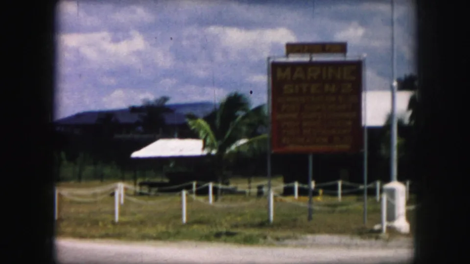1959 8mm frame of the Marine Site No. 2 roadside sign in Kansas City, Missouri, with palm trees and low buildings beyond.