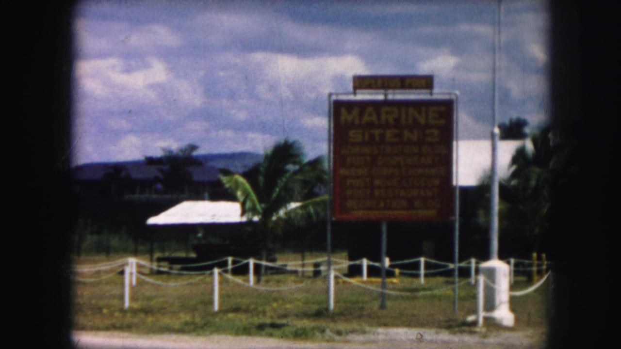 Large sign beside rope posts and a flagpole near grass and trees.