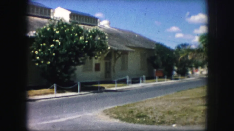 1959 8mm view of a quiet Kansas City road curving beside a pale building and leafy landscaping.