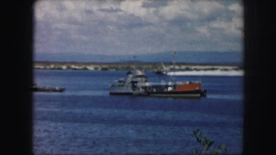 1959 8mm frame from the Kansas City, Missouri metadata set showing a ferry or workboat on calm water beneath a cloudy sky.