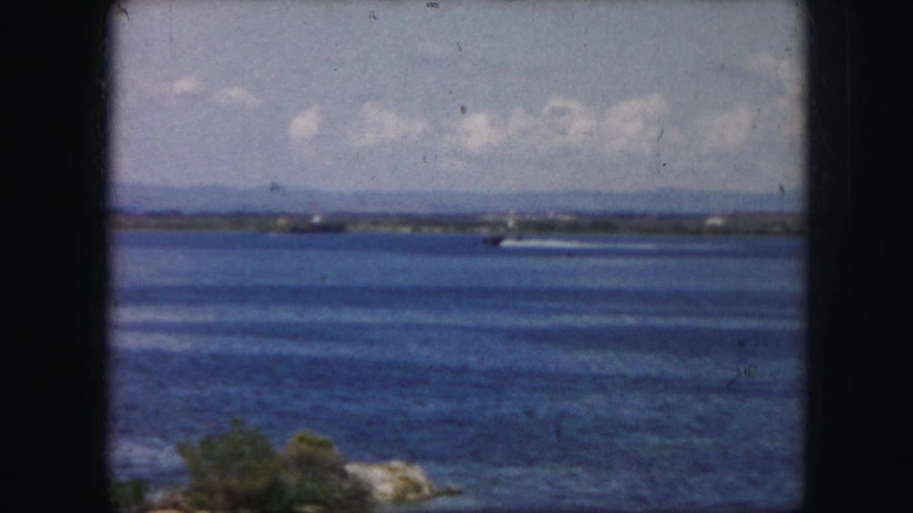 Blue lake with distant shoreline, clouds, and a small boat wake across the water.