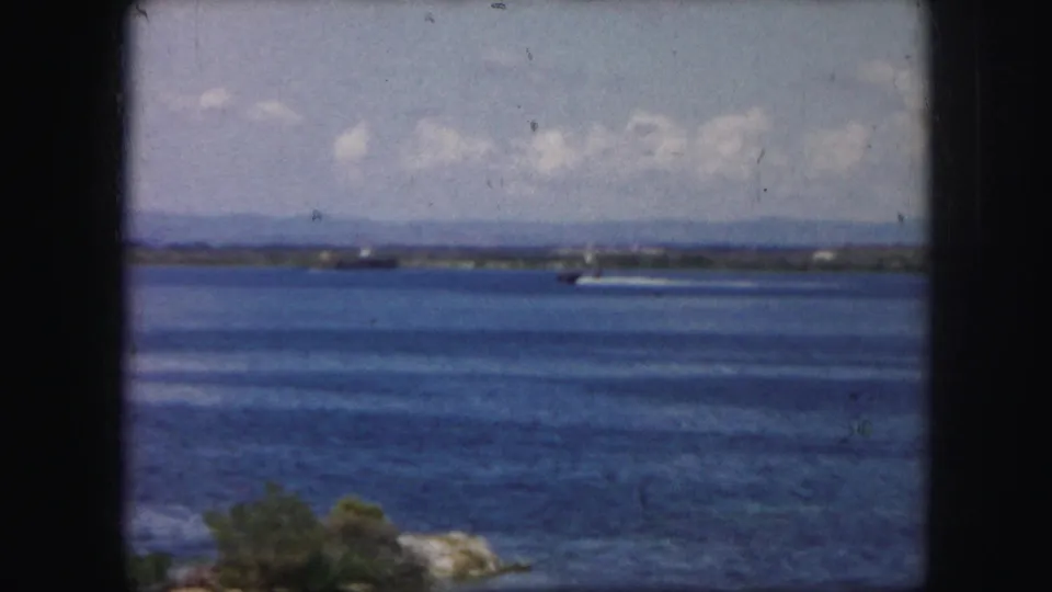 1959 Kansas City home-movie frame showing a blue lake, distant shore, partly cloudy sky, and a small speedboat wake.
