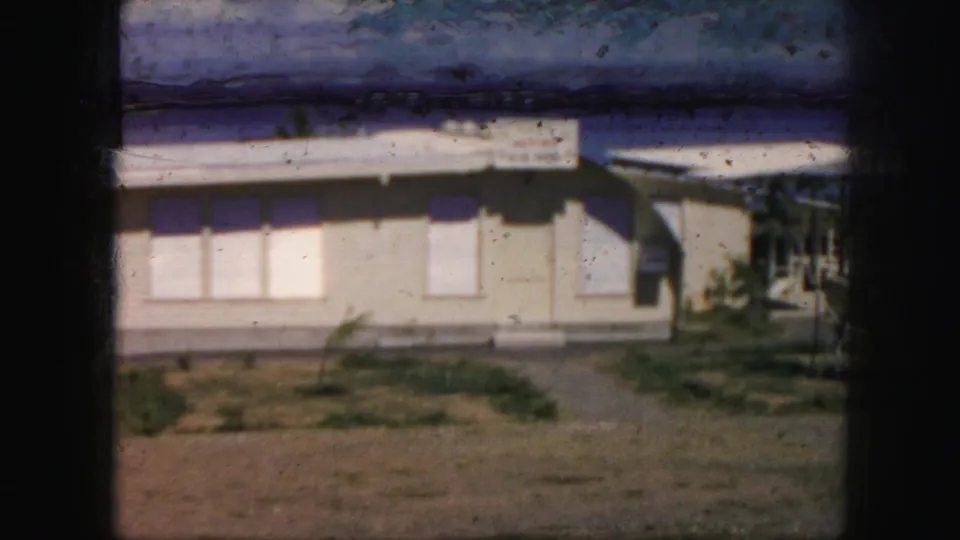 1959 Kansas City lakeside frame showing a low light-colored building, closed windows, sparse landscaping, and water behind it.